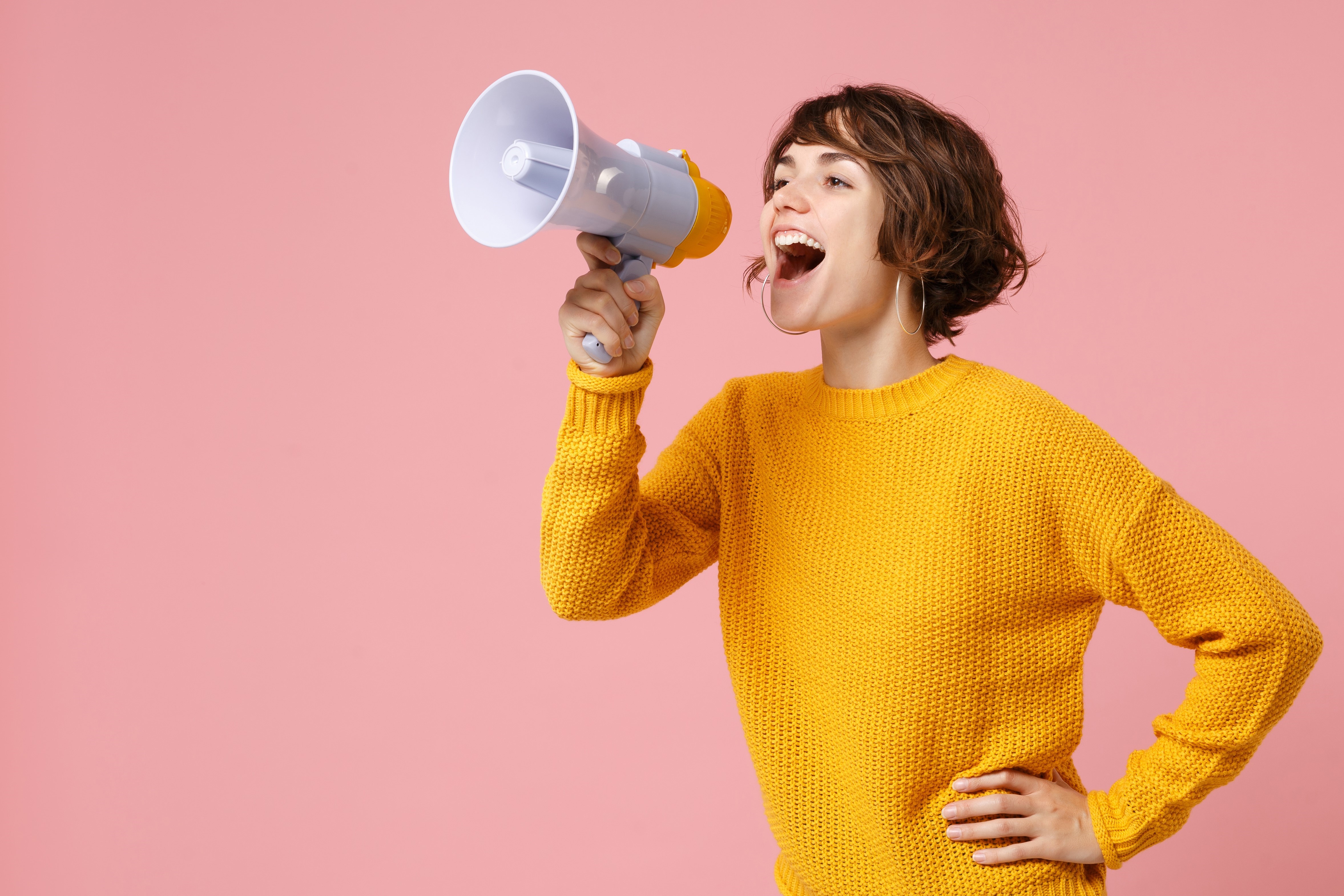 Woman in yellow jumper with megaphone on pink background