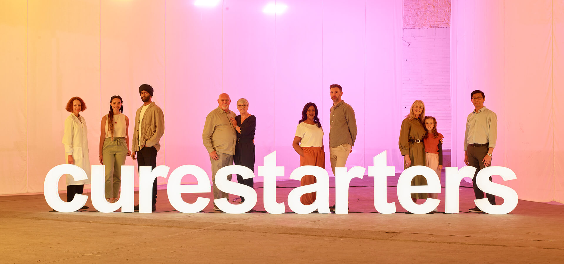 A group of people standing in front of large light installation of the word curestarters